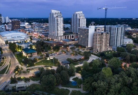 Aerial view of downtown London, Ontario at dusk, showing city buildings, streets, green space, and the Thames River.