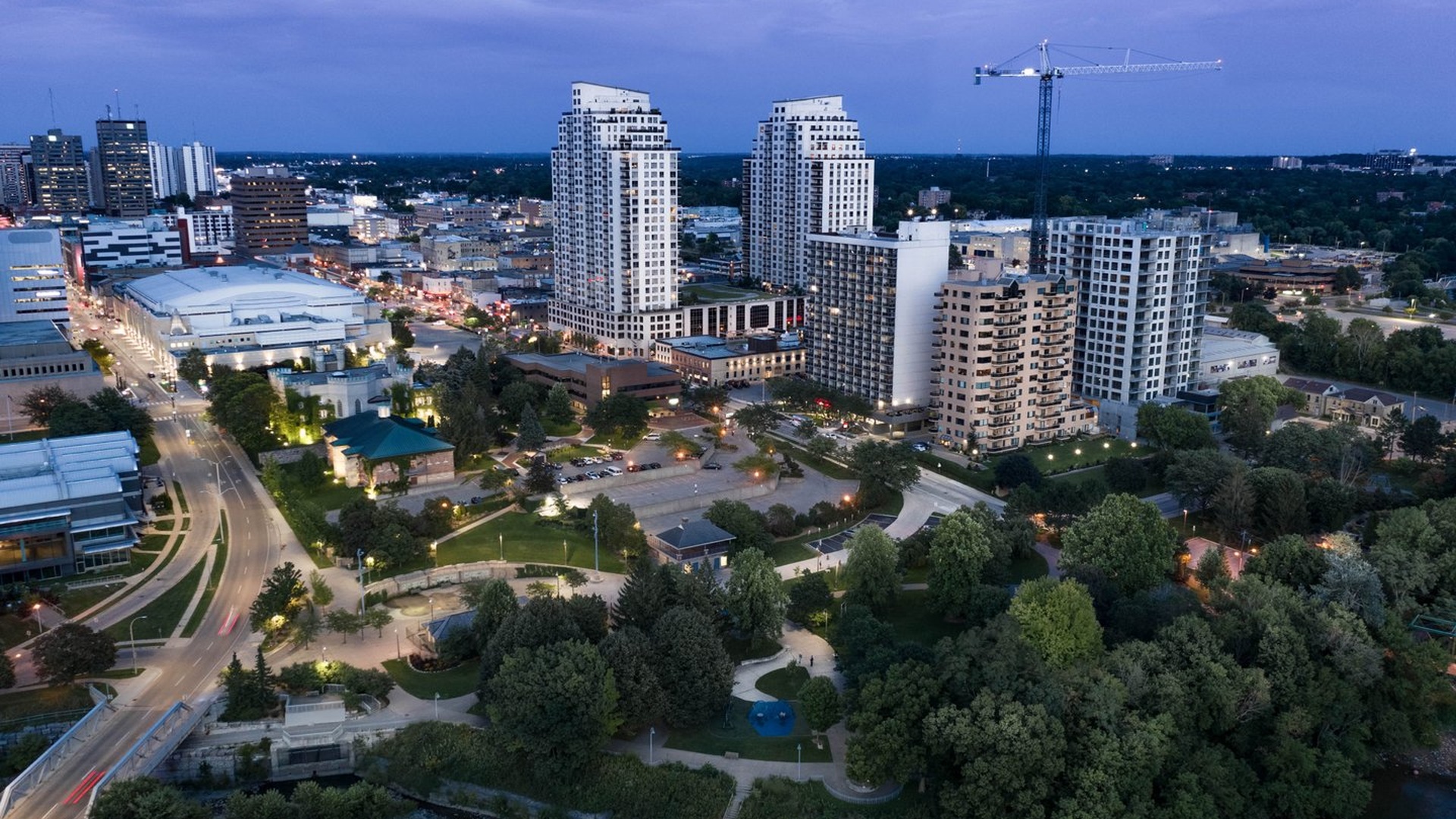 Aerial view of downtown London, Ontario at dusk, showing city buildings, streets, green space, and the Thames River.